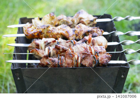 Grilling meat shashlik on skewers outdoors at a summer gathering Grilling meat shashlik on skewers outdoors at a summer gathering 141087006
