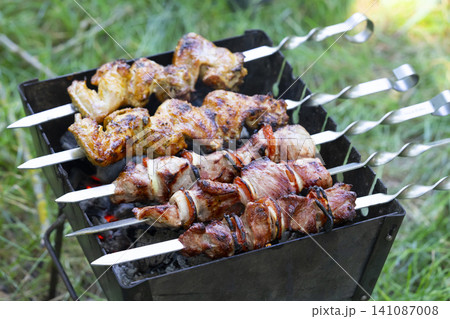 Grilling delicious shashlik on a mangal during a sunny outdoor gathering Grilling delicious shashlik on a mangal during a sunny outdoor gathering 141087008