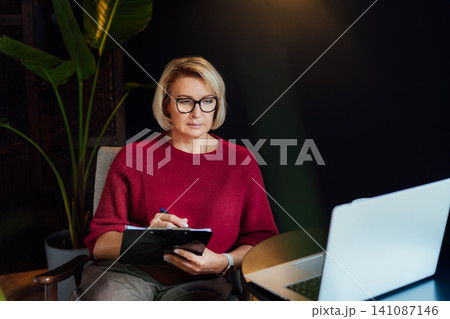 Concentrated 50's stylish, confident mature businesswoman, middle aged experienced senior female professional, business coach, mentor, therapist, counselor working on laptop in office. Female leader Concentrated 50's stylish, confident mature businesswoman, middle aged experienced senior female professional, business coach, mentor, therapist, counselor working on laptop in office. Female leader 141087146