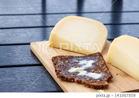 Sourdough wholegrain rye bread with melting butter, served with cheese on a wooden board. Sourdough wholegrain rye bread with melting butter, served with cheese on a wooden board. 141087859