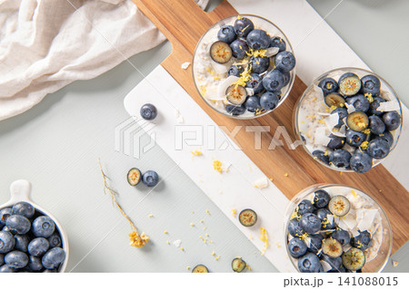 Three healthy blueberry Lemon Overnight Oats topped with blueberries, lemon zest and coconut shavings on a light blue wooden counter. Top view Three healthy blueberry Lemon Overnight Oats topped with blueberries, lemon zest and coconut shavings on a light blue wooden counter. Top view 141088015