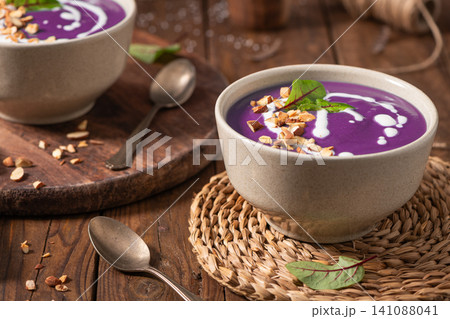 Healthy creamy red cabbage soup topped with herbs, a swirl of cream, toasted almonds, and fresh herbs, resting on a rustic wooden board. Healthy creamy red cabbage soup topped with herbs, a swirl of cream, toasted almonds, and fresh herbs, resting on a rustic wooden board. 141088041