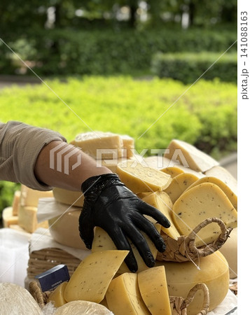 Cheese market with gloved hand reaching for stacked assortment of various cheese blocks 141088163