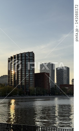 City skyline at sunset with reflections on buildings by river and cloudy sky background City skyline at sunset with reflections on buildings by river and cloudy sky background 141088172