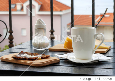 Balcony breakfast with coffee bread cheese and sugar dispenser. Mediterranean travel lifestyle scene with red rooftops in background Balcony breakfast with coffee bread cheese and sugar dispenser. Mediterranean travel lifestyle scene with red rooftops in background 141088296