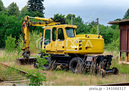 Yellow road rail excavator parked on abandoned overgrown railroad track in summer Yellow road rail excavator parked on abandoned overgrown railroad track in summer 141088317