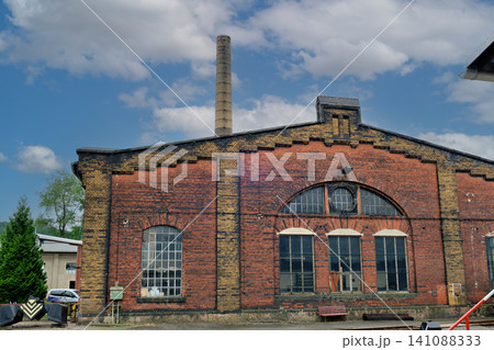 Historical Red Brick Railway Depot Building Facade with Arched Windows and Tall Industrial Chimney Historical Red Brick Railway Depot Building Facade with Arched Windows and Tall Industrial Chimney 141088333