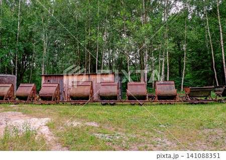 Row of old rusty narrow gauge mining dump carts standing near a wooden shed in forest Row of old rusty narrow gauge mining dump carts standing near a wooden shed in forest 141088351