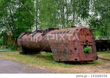Abandoned rusty steam locomotive boiler body resting on the ground near green trees Abandoned rusty steam locomotive boiler body resting on the ground near green trees 141088356