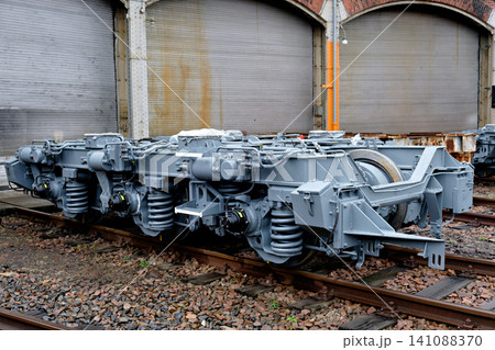 Grey train bogie wheelset assembly with metal springs on a gravel railway track 141088370
