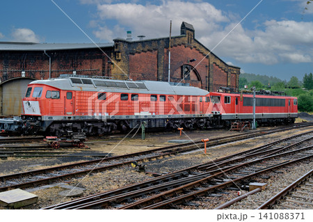 Two classic red diesel locomotives on multiple tracks outside a historic brick train station Two classic red diesel locomotives on multiple tracks outside a historic brick train station 141088371
