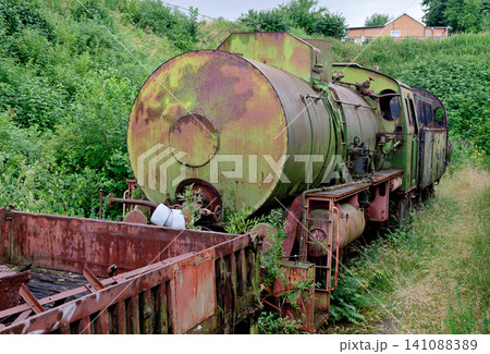Rusty old steam locomotive engine abandoned in an overgrown green field 141088389