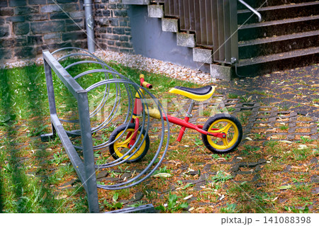 Small red and yellow child balance bicycle parked in a spiral metal stand outdoors Small red and yellow child balance bicycle parked in a spiral metal stand outdoors 141088398
