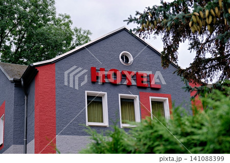 Hotel building facade with red sign seen through green pine tree branches 141088399