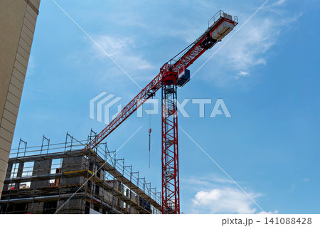 Large red industrial construction crane building a new house under blue sky Large red industrial construction crane building a new house under blue sky 141088428
