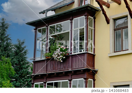 Elegant dark wooden enclosed balcony veranda decorated with blooming pink flowers on a villa facade Elegant dark wooden enclosed balcony veranda decorated with blooming pink flowers on a villa facade 141088483
