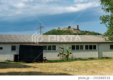 Agricultural farm building with machinery and historic castle ruin on hill in background Agricultural farm building with machinery and historic castle ruin on hill in background 141088518