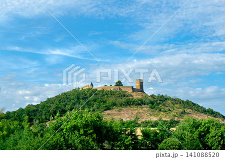 Historic medieval castle fortress ruins standing on top of a lush green hill under blue sky Historic medieval castle fortress ruins standing on top of a lush green hill under blue sky 141088520