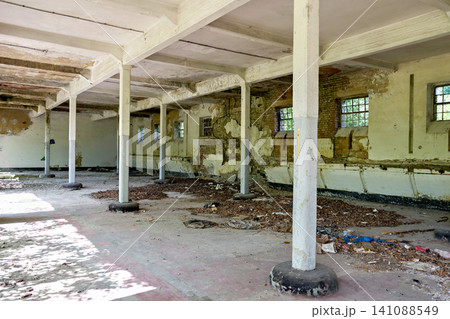 Long empty hall of abandoned industrial building with concrete pillars and litter Long empty hall of abandoned industrial building with concrete pillars and litter 141088549