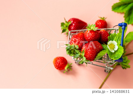 strawberries in small grocery cart on light pink background strawberries in small grocery cart on light pink background 141088631
