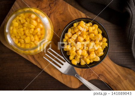 Bowl Of Sweet Corn Kernels With Fork On Wooden Cutting Board Next To Jar 141089043