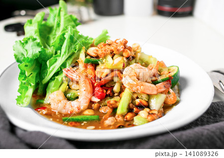 Delicious papaya salad with shrimp boil tentacles, Lentils, nuts, raw papaya, fish sauce, sugar, tomato, and lime. Cutlery is placed on the wooden floor. Taken in a photo studio. Thai food. 141089326