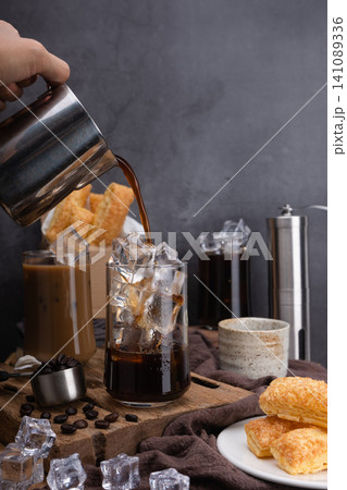 Pour milk make latte coffee, Asian iced coffee in transparent glass and roasted coffee beans and Crispy Pie on wood. black background studio photo, Copy space for your text Pour milk make latte coffee, Asian iced coffee in transparent glass and roasted coffee beans and Crispy Pie on wood. black background studio photo, Copy space for your text 141089336