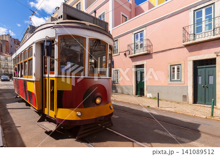 Classic yellow tram traveling through a historic street in Lisbon, Portugal, surrounded by traditional residential buildings and urban architecture. Classic yellow tram traveling through a historic street in Lisbon, Portugal, surrounded by traditional residential buildings and urban architecture. 141089512
