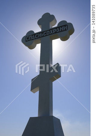 Orthodox cross against the blue sky and the sun. Cross in the backlight of the sun. Symbol of the Christian faith. The inscription on the cross: salvation and preservation Orthodox cross against the blue sky and the sun. Cross in the backlight of the sun. Symbol of the Christian faith. The inscription on the cross: salvation and preservation 141089735