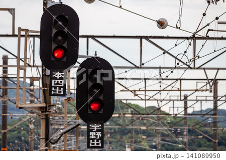 赤信号が点灯する鉄道の出発信号機と架線柱のクローズアップ 赤信号が点灯する鉄道の出発信号機と架線柱のクローズアップ 141089950