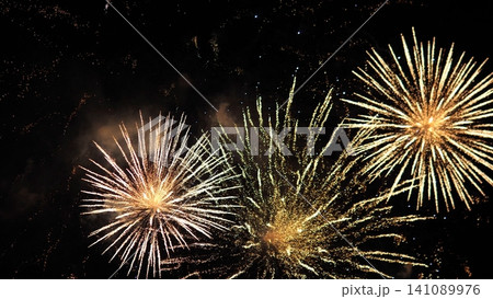 Golden fireworks explode across dark night sky, filling scene with radiant starbursts, sparkling trails, drifting smoke and festive celebration mood for outdoor spectacle Golden fireworks explode across dark night sky, filling scene with radiant starbursts, sparkling trails, drifting smoke and festive celebration mood for outdoor spectacle 141089976
