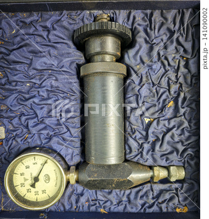 A manual pump tool with a pressure gauge sits inside a blue lined storage case. The tool shows wear from use and is ready for various tasks and projects. A manual pump tool with a pressure gauge sits inside a blue lined storage case. The tool shows wear from use and is ready for various tasks and projects. 141090002