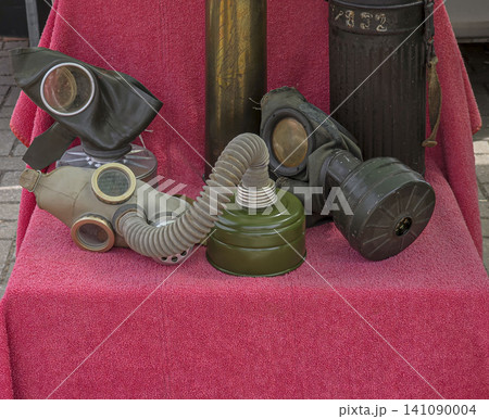 Various World War II military gas masks and filter canisters are arranged on a red surface. This display highlights the historical significance of these items. Various World War II military gas masks and filter canisters are arranged on a red surface. This display highlights the historical significance of these items. 141090004