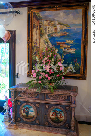 Antique cabinet with flowers beneath large framed painting Antique cabinet with flowers beneath large framed painting 141090249