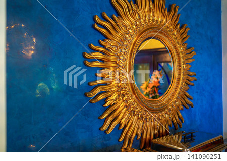 Golden sunburst mirror on bright blue textured wall 141090251
