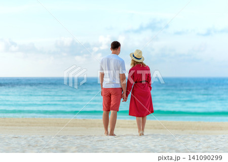Young couple holding hands walking on white sand toward turquoise ocean Young couple holding hands walking on white sand toward turquoise ocean 141090299