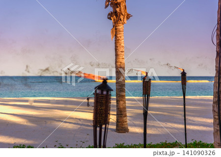 Tiki torches burning on tropical beach at dusk Tiki torches burning on tropical beach at dusk 141090326