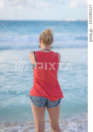 Blonde woman standing barefoot on tropical beach shore Blonde woman standing barefoot on tropical beach shore 141090327