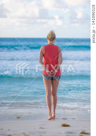 Blonde woman standing barefoot on tropical beach shore Blonde woman standing barefoot on tropical beach shore 141090328