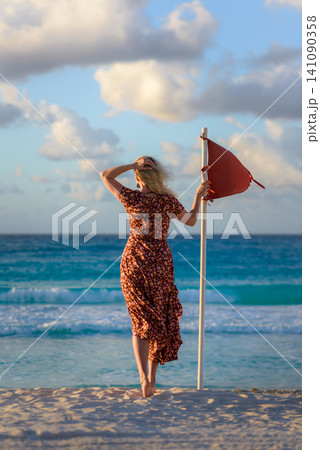 Woman holding red flag on tropical beach at sunset Woman holding red flag on tropical beach at sunset 141090358