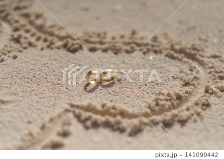 Golden wedding rings inside heart drawn on tropical sand Golden wedding rings inside heart drawn on tropical sand 141090442