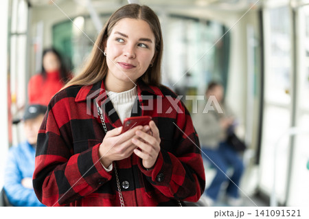 Girl is standing with phone in tram car, getting to work Girl is standing with phone in tram car, getting to work 141091521