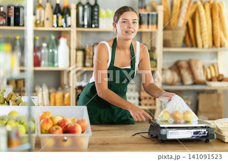 Young woman seller weighs apples in bag Young woman seller weighs apples in bag 141091523