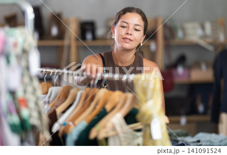 Young woman comes to boutique and looks at clothes Young woman comes to boutique and looks at clothes 141091524