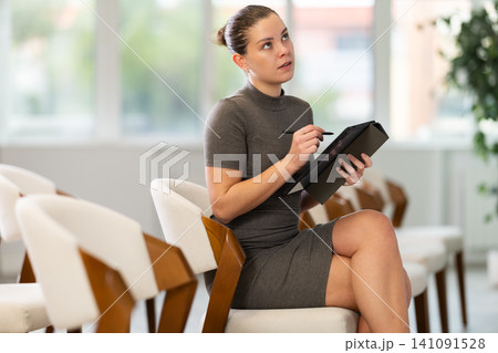 During lecture, young woman listener makes notes on tablet During lecture, young woman listener makes notes on tablet 141091528