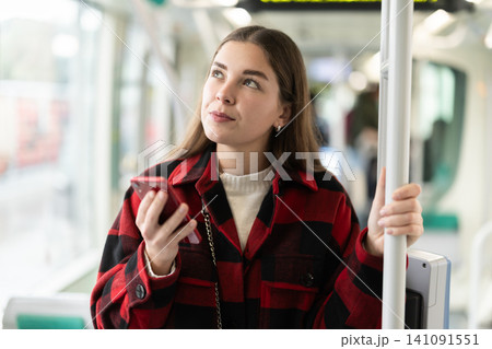 Girl with long hair standing in tram with phone Girl with long hair standing in tram with phone 141091551