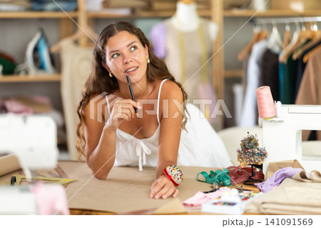 Female dress designer drawing patterns for garment in studio 141091569