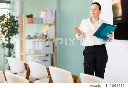 Young woman coach presenting in auditorium with folder 141091612