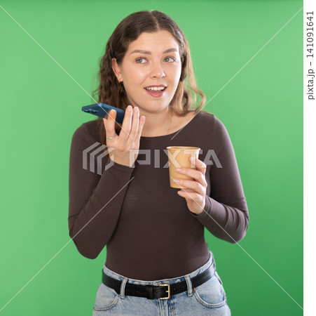 Young girl with coffee on green screen background records voice message Young girl with coffee on green screen background records voice message 141091641