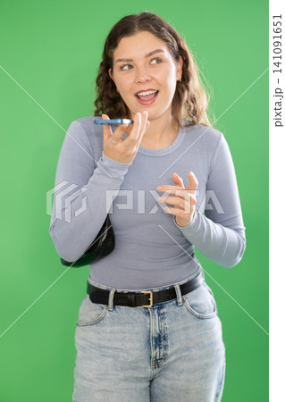 Young woman recording voice message in front of green screen 141091651